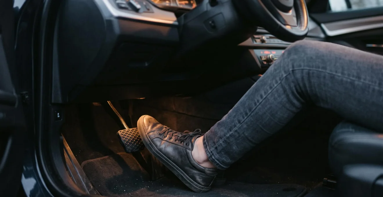Gros plan sur une main appuyant sur la pédale de frein d'une voiture dans un garage, symbolisant la vigilance face à l'usure des freins