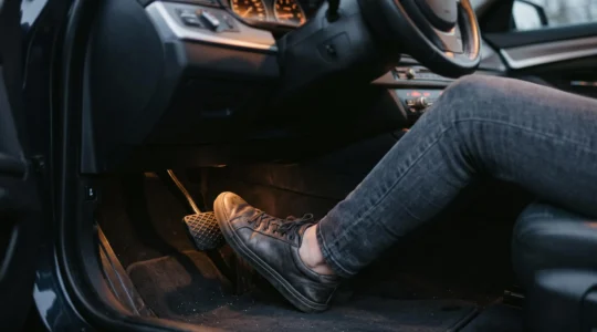 Gros plan sur une main appuyant sur la pédale de frein d'une voiture dans un garage, symbolisant la vigilance face à l'usure des freins